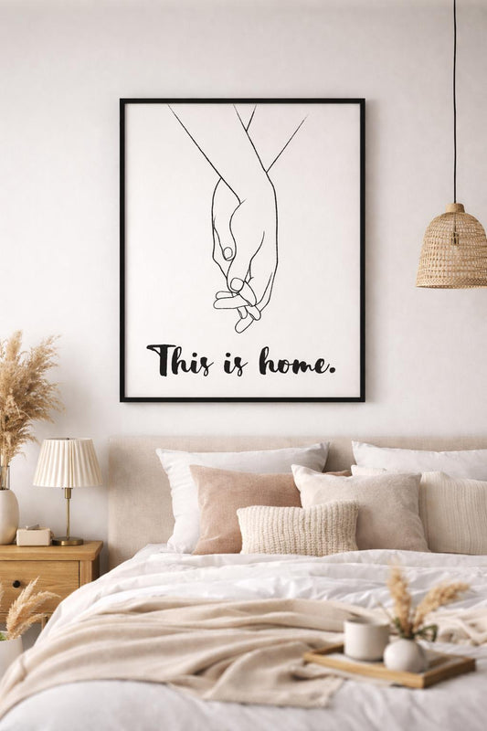 Beyaz arka planda siyah çerçeveli "This is Home" yazılı minimalist el ele tutuşan çift tablosu.